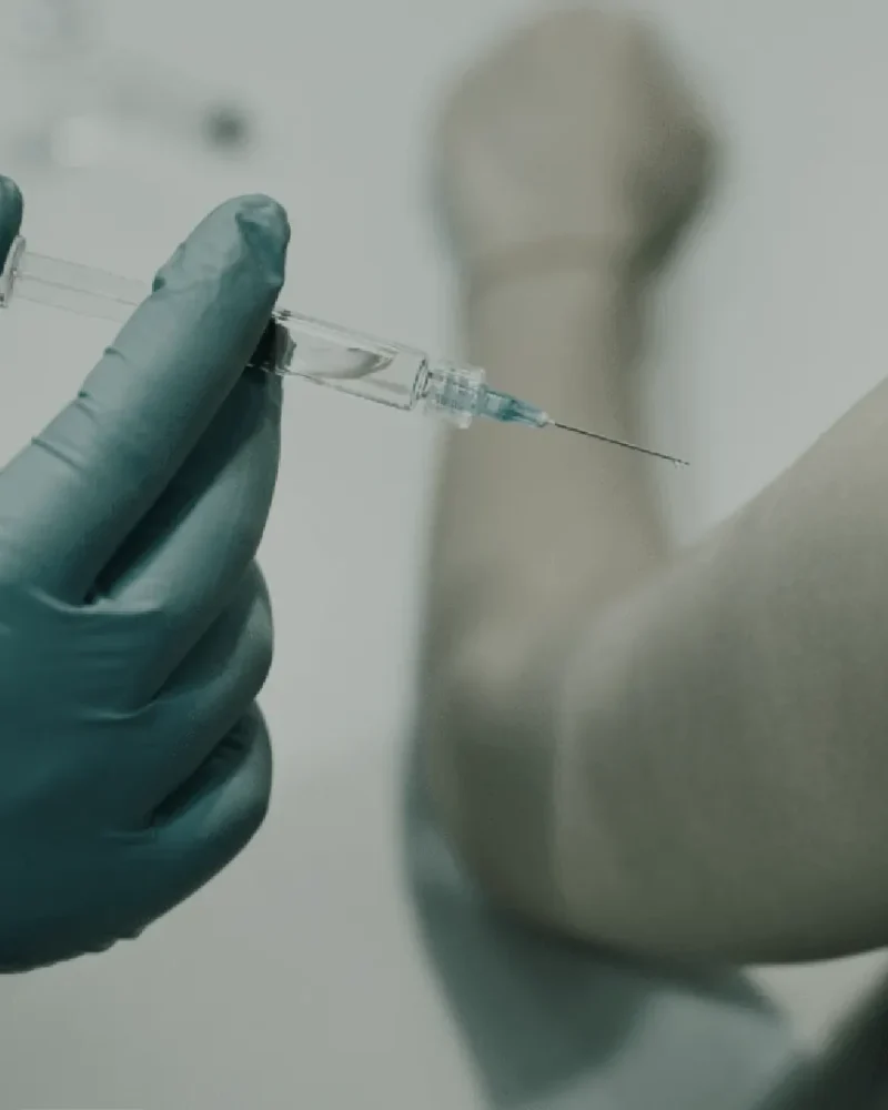 Gloved hands preparing a vitamin injection in a syringe